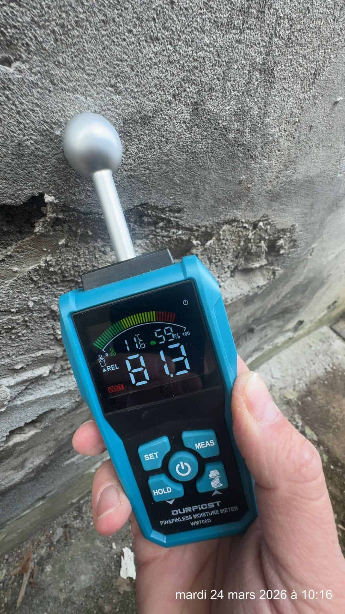 mesure d'humidité par testeur électronique sur mur extérieur dégradé avec décollement d'enduit, vue rapprochée du contrôle