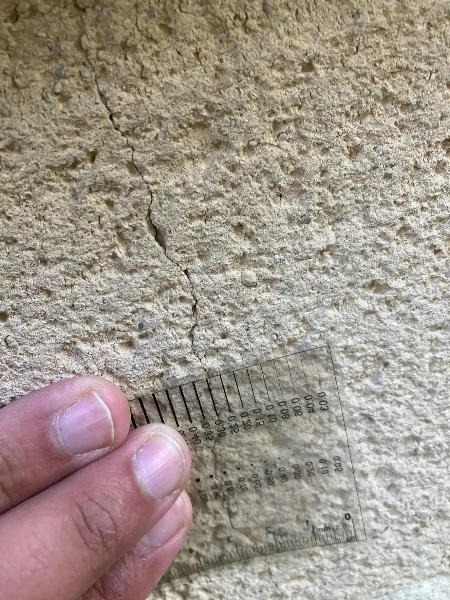 Mesure d'une fissure fine sur enduit de façade avec une règle de précision, relevé réalisé lors d'un audit avant achat.