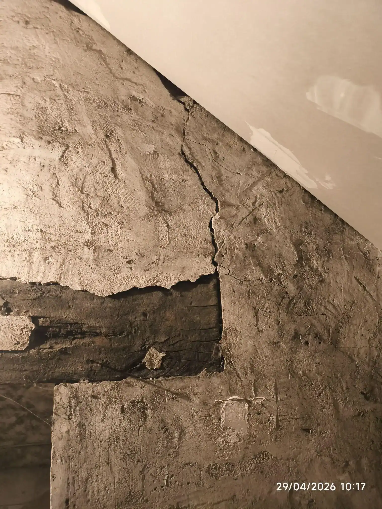 Fissure verticale sur mur en enduit au droit d'un linteau bois apparent, désordre structurel visible en grenier.