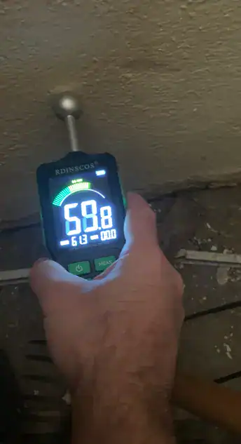Humidimètre appliqué sur une paroi en pied de mur pour mesurer le taux d'humidité au-dessus d'une dalle béton.