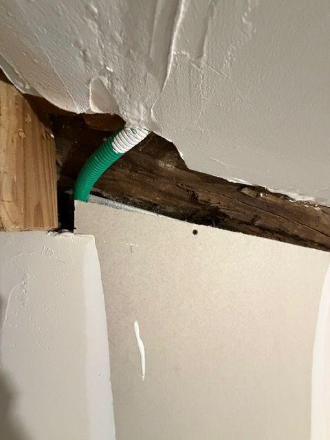 Gaine électrique verte traversant une cloison en plâtre, finition grossière à contrôler après un dommage électrique.