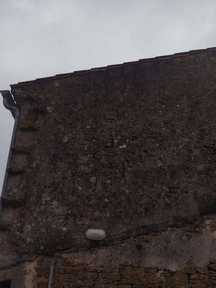 Fissures et trous de scellement en haut d'un pignon en pierre, anciens appuis de charpente sous la toiture.
